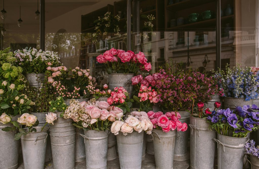 Flower shop storefront with buckets of pink roses, purple flowers, and mixed blooms