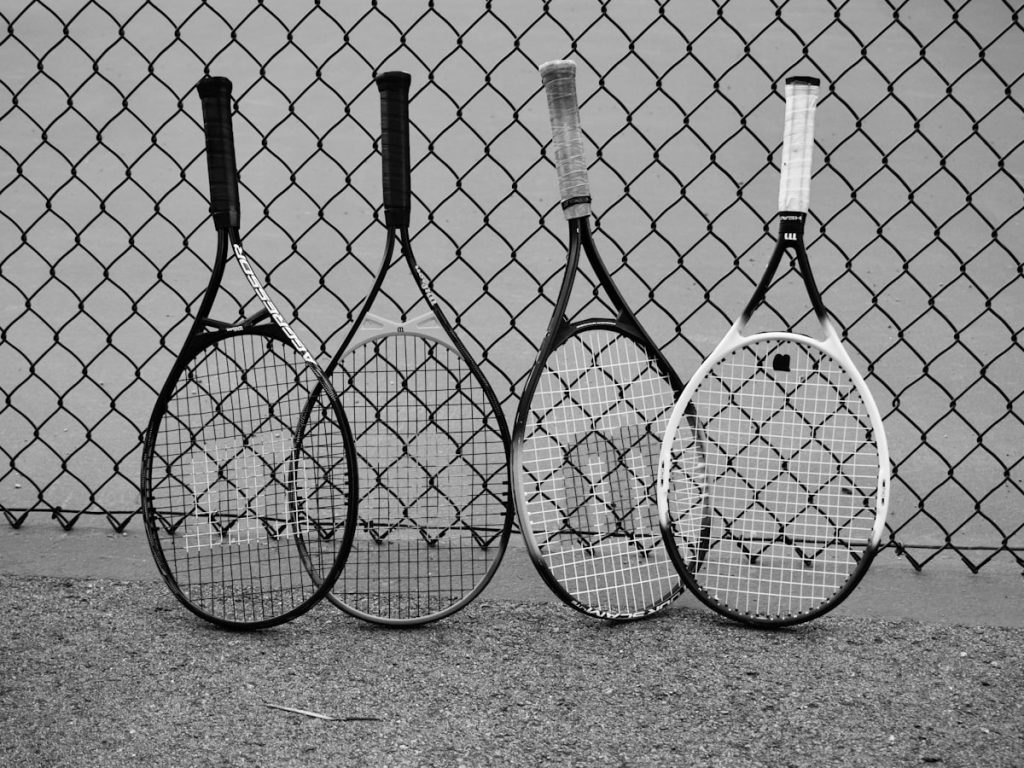 Four tennis rackets leaning against a fence
