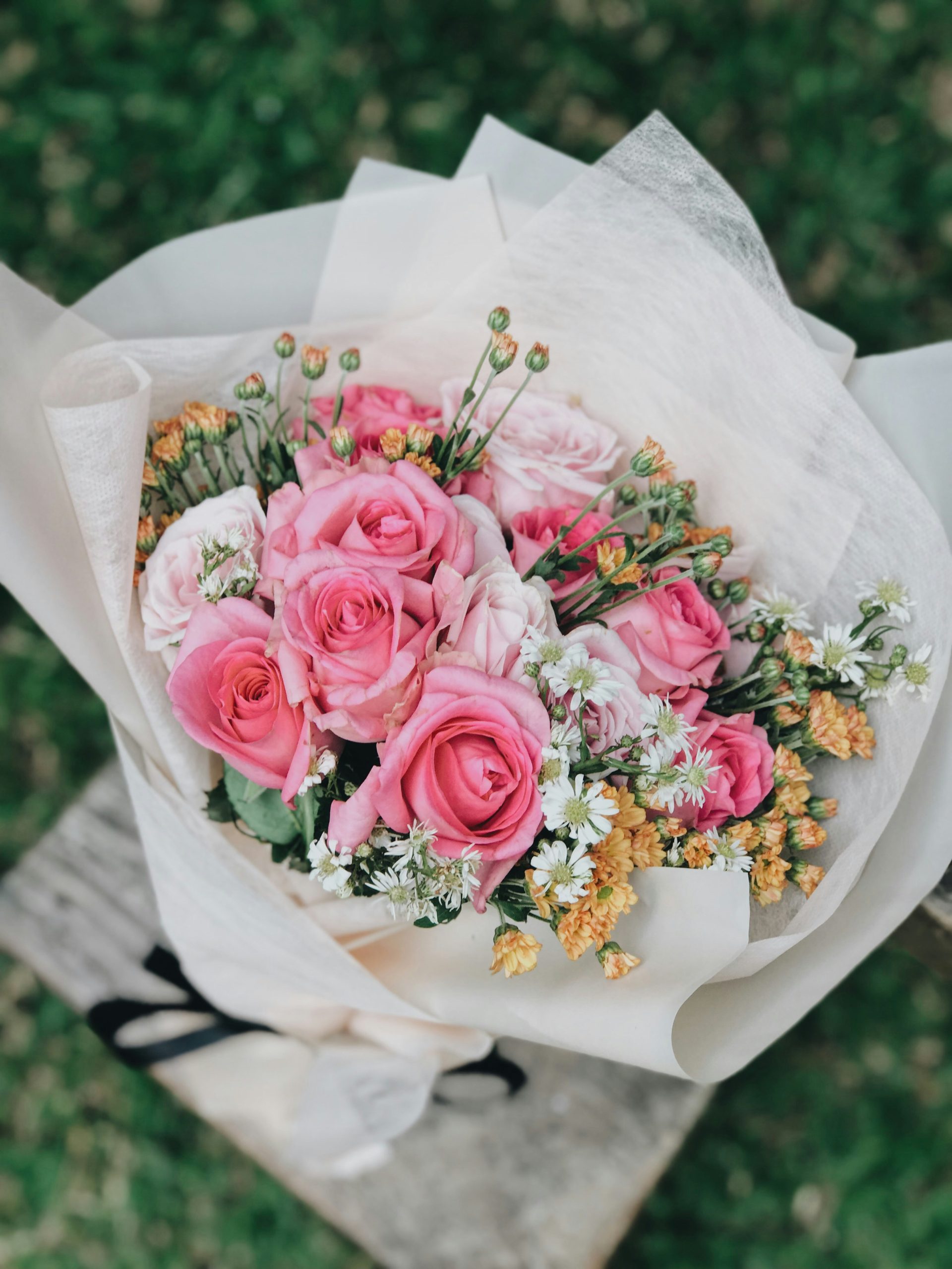 Pink roses wrapped in white tissue paper with small wildflowers