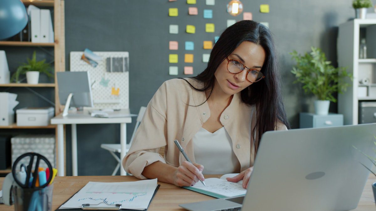 Woman working at a desk with a laptop and notebook