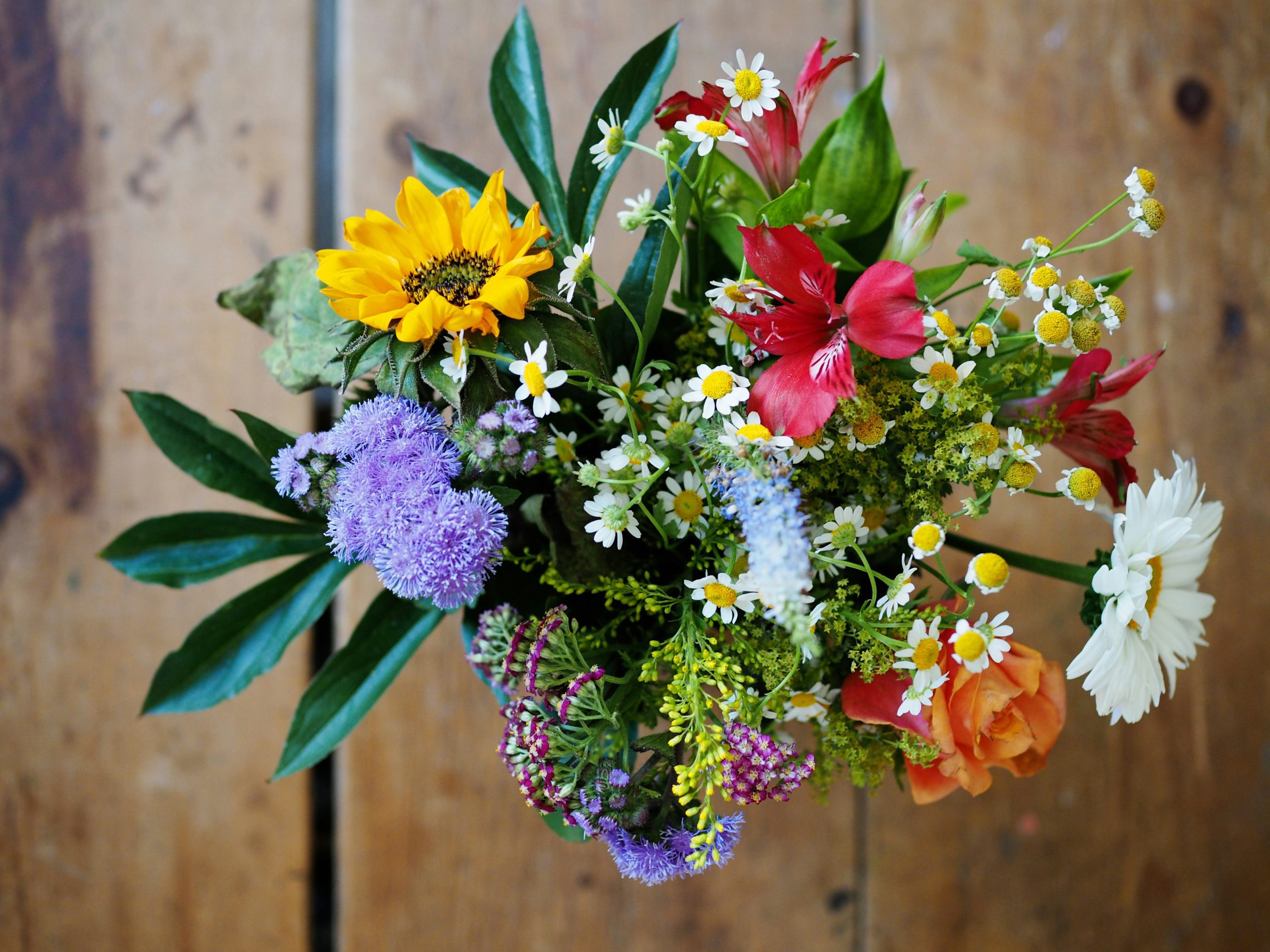 Colorful wildflower bouquet with sunflower, daisies, and alstroemeria on rustic wood