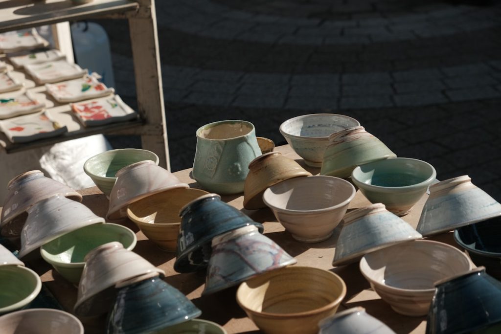 Assortment of handmade ceramic bowls and cups displayed outdoors