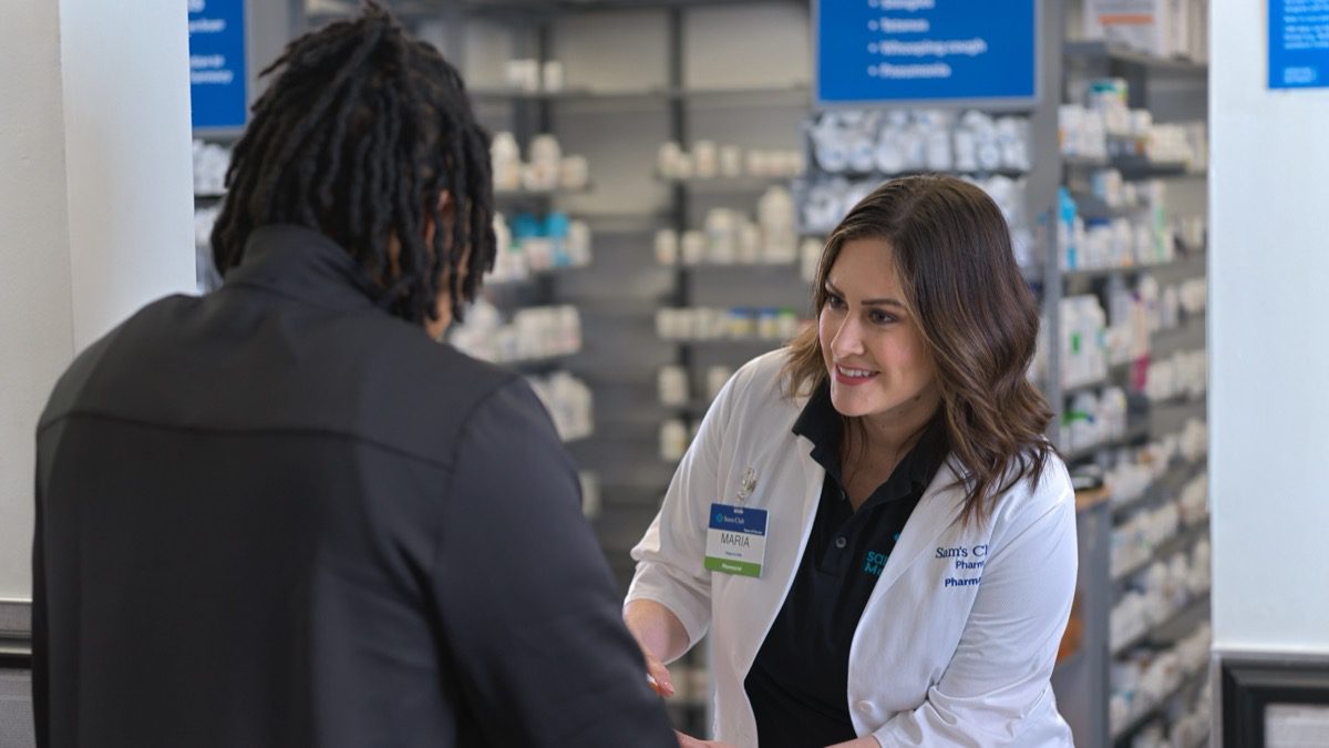 A Sam's Club pharmacist in a white coat helping a member at the pharmacy counter