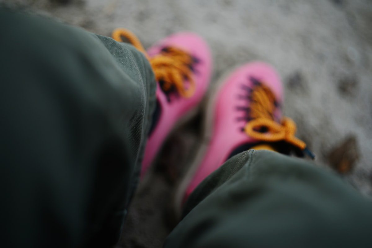 Pink sneakers with orange laces on feet.