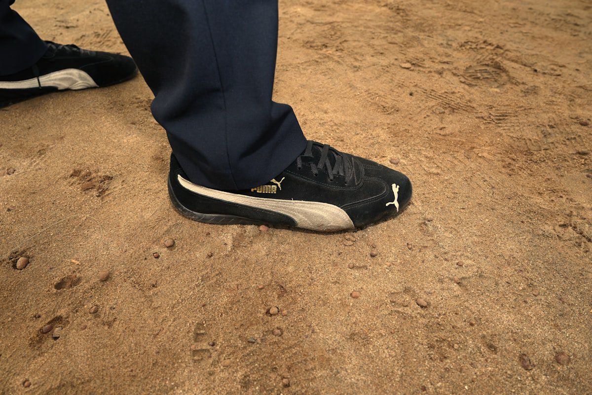Close-up of a person wearing black puma sneakers on dirt.
